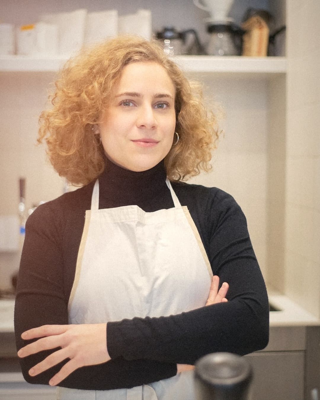 A café owner in an apron, arms crossed, smiling