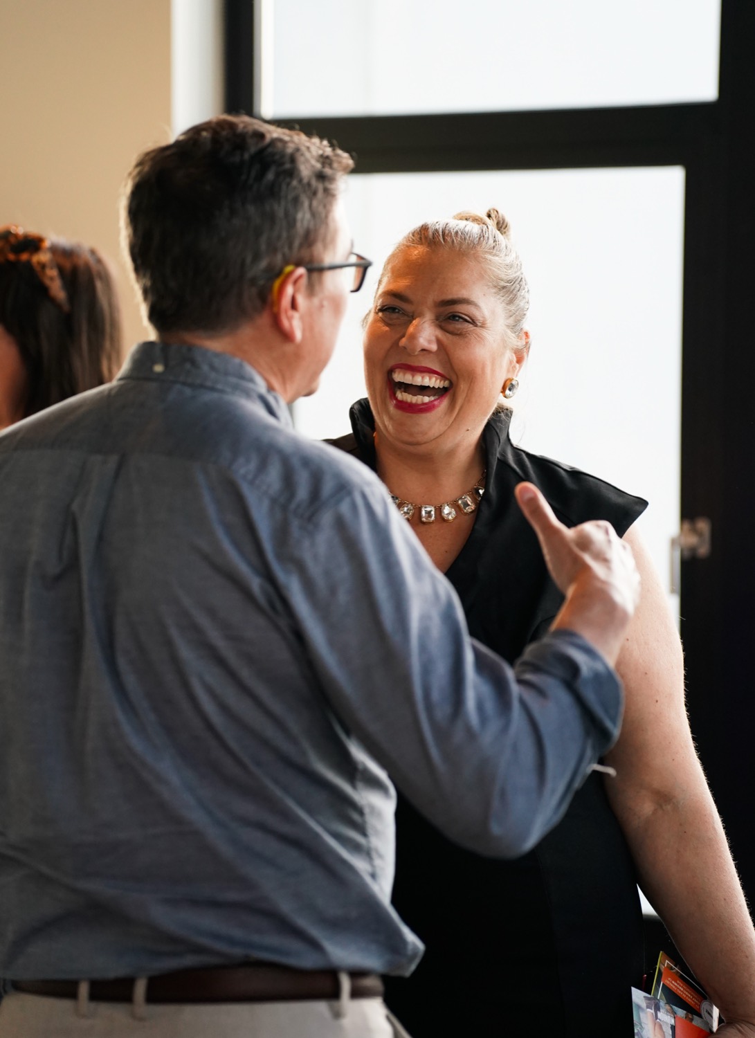 Two guests mid-conversation by the windows at the Vantage launch party